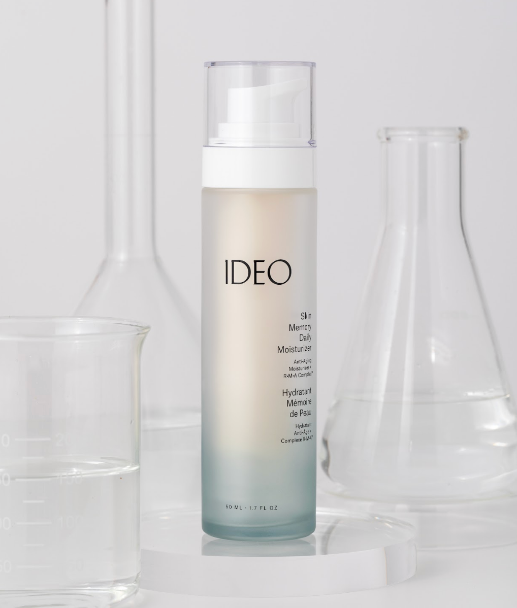 50ml glass bottle of age-defying IDEO Skin Memory Daily Moisturizer in air pump with clear cap in front of glass science instruments