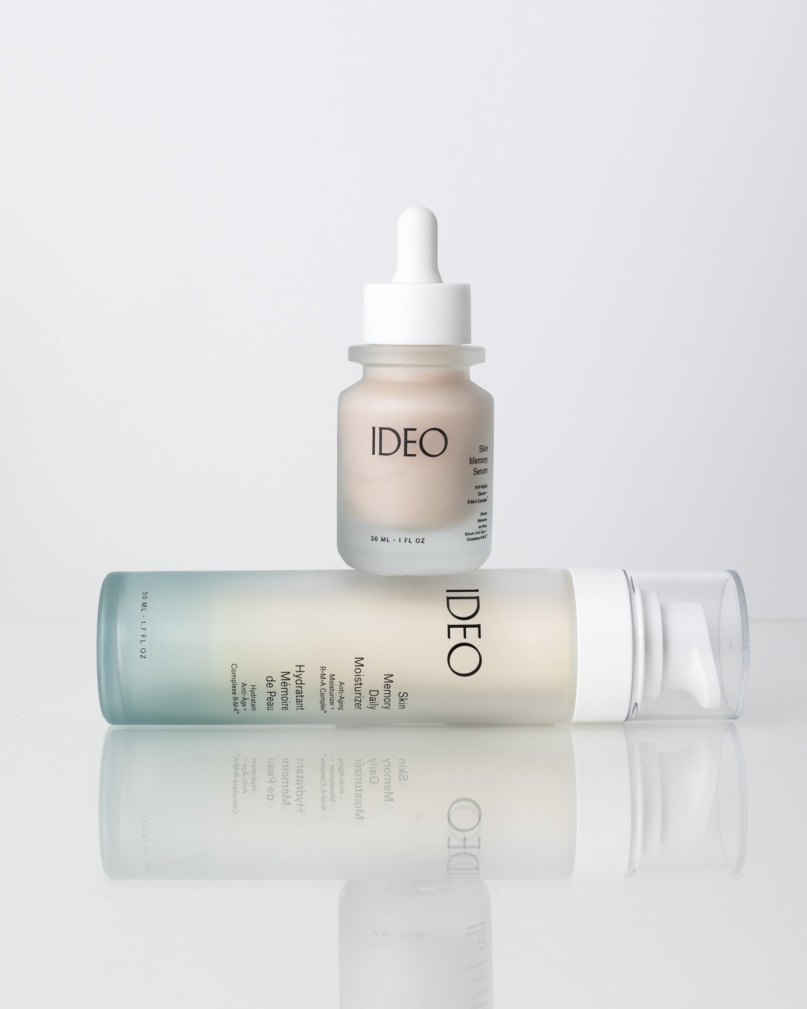 Bottle of Skin Memory Serum sitting atop a horizontal bottle of Skin Memory Moisturizer