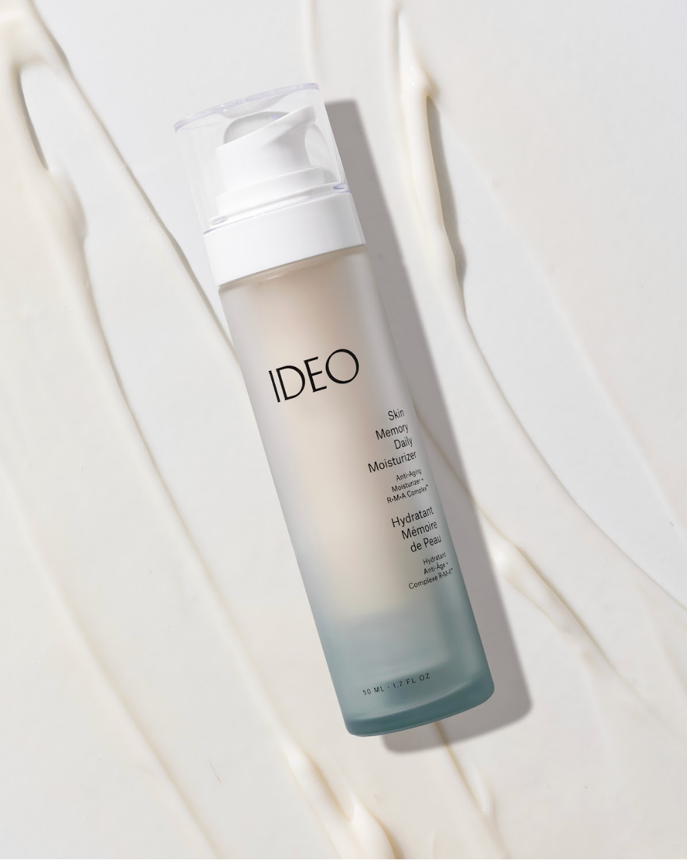 IDEO Skin Memory Daily Moisturizer frosted pump bottle lying beside cream texture swatch flat lay editorial