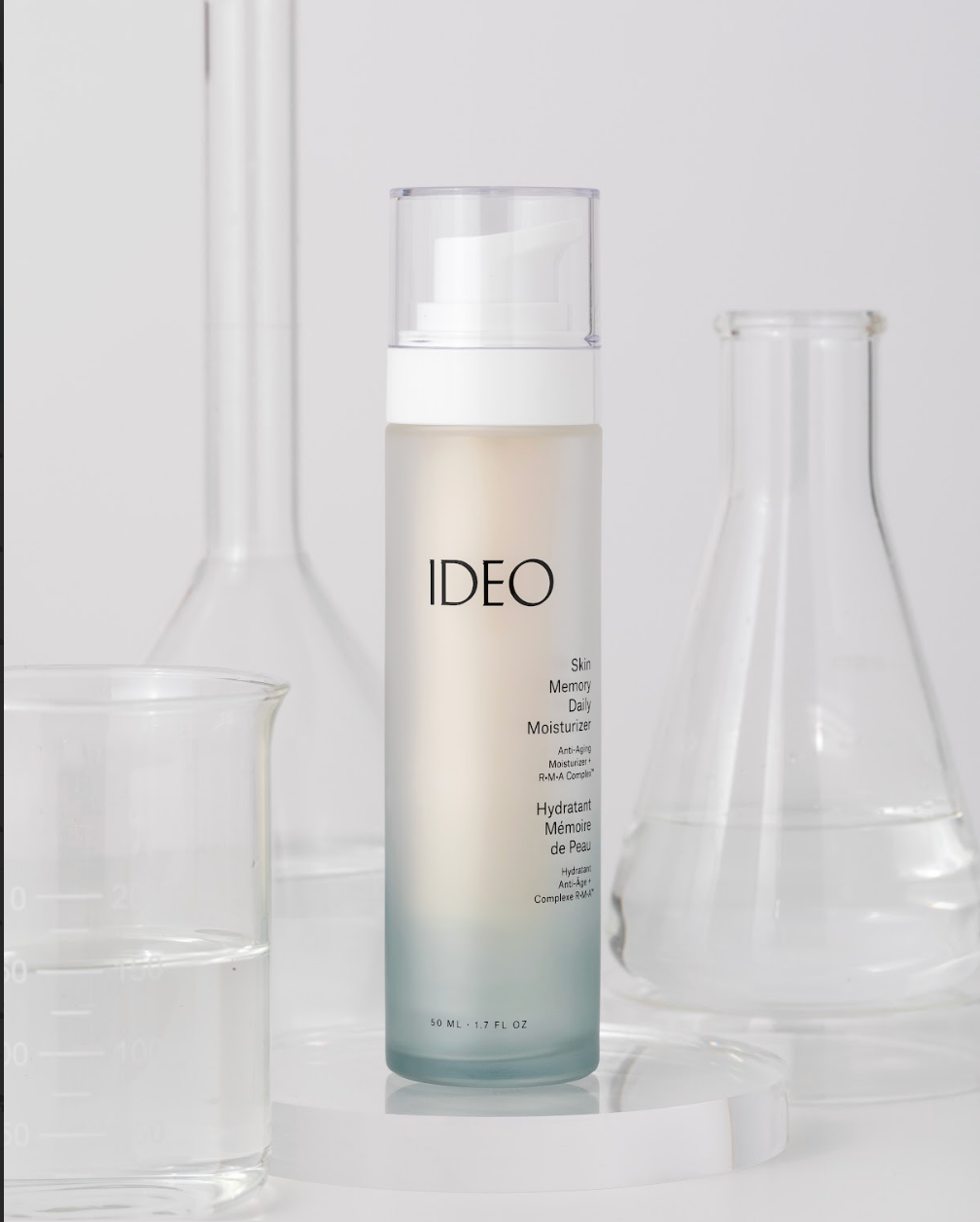 IDEO Skin Memory Daily Moisturizer bottle surrounded by glass laboratory flasks science-forward editorial shot