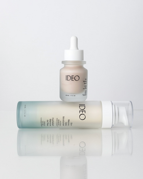 IDEO Skin Memory Serum dropper bottle balanced on top of IDEO Skin Memory Daily Moisturizer pump bottle on white reflective surface Power Duo editorial