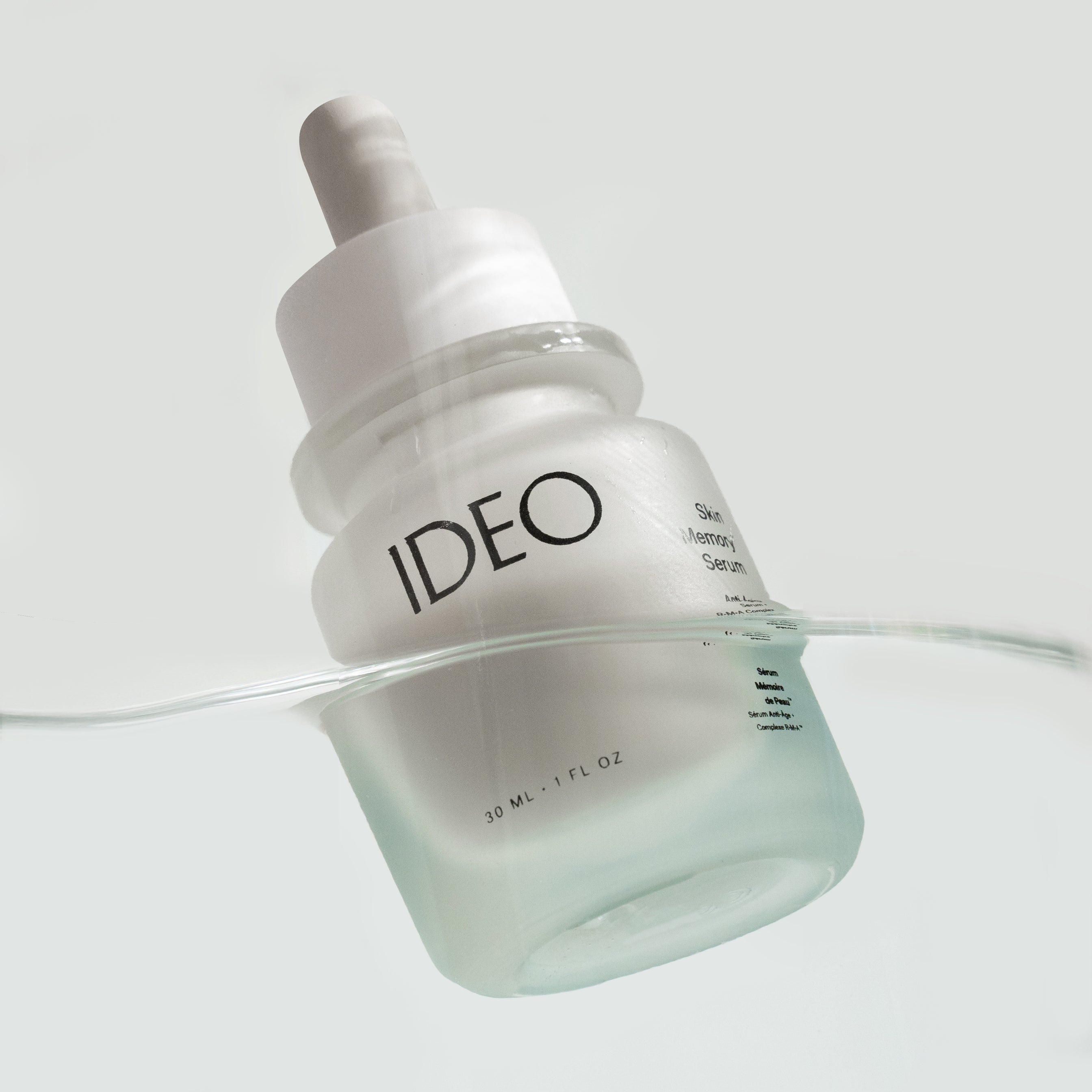 White skincare serum bottle with 'IDEO' branding on a light gray background